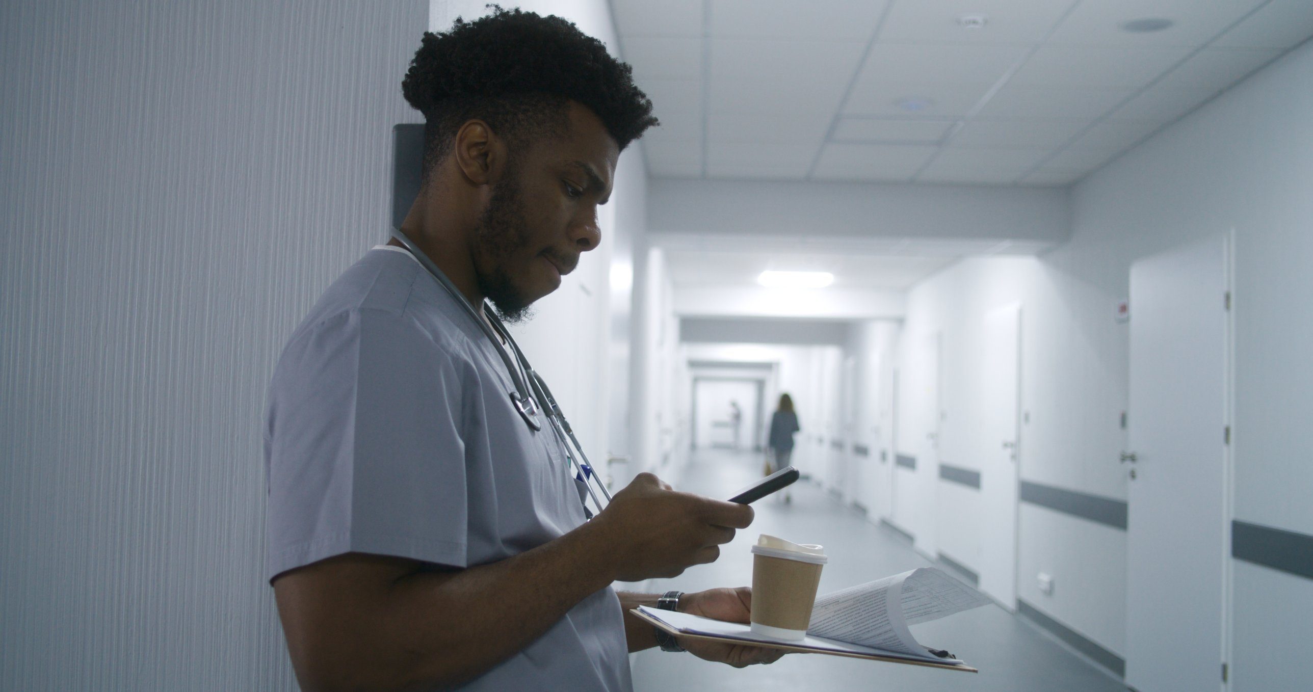 A healthcare worker checking his phone in a hospital corridor